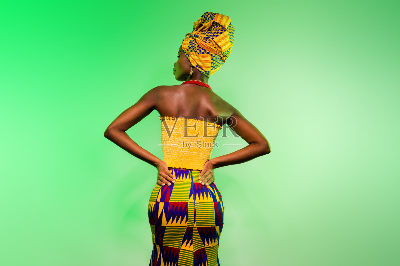 一位迷人的瘦弱女性，双手叉腰，从后方回望，在明亮的浅绿色背景前摆出造型照片摄影图片