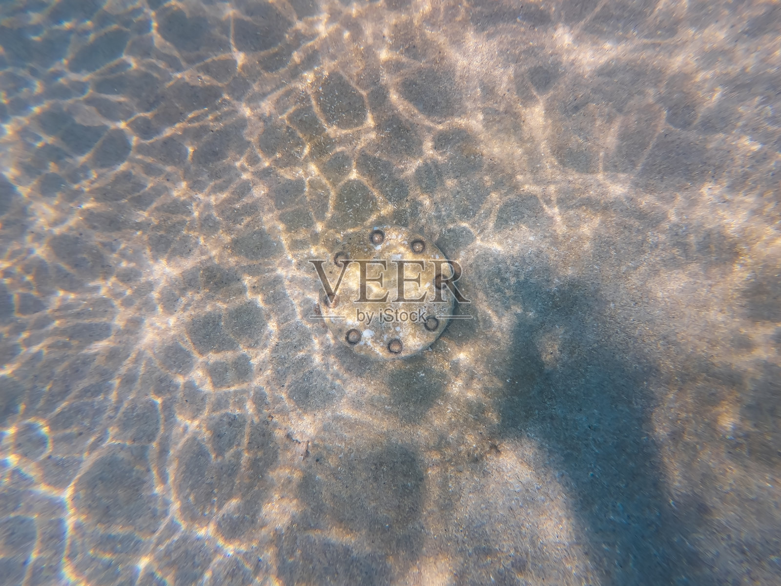 海底管道上一个神秘的带螺栓的金属法兰，静卧在沙质的海底，阳光在其上投下闪烁的光斑。照片摄影图片