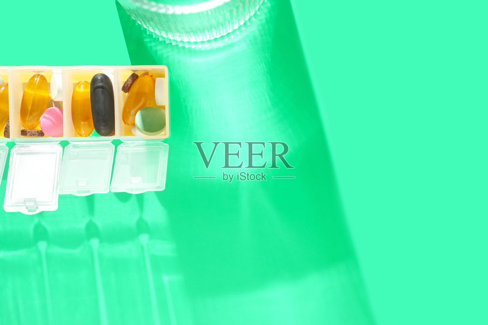 五颜六色的药丸收纳盒，里面装有各种补充剂和药物，背景是鲜艳的绿色。照片摄影图片