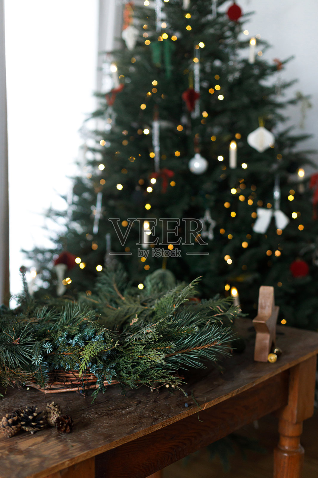 制作圣诞花环。圣诞花环由冷杉、松树和雪松枝条、剪刀组成，摆放在乡村风格的星星旁，背景是时尚的圣诞树，桌子是木质的。冬季节日准备和装饰。照片摄影图片