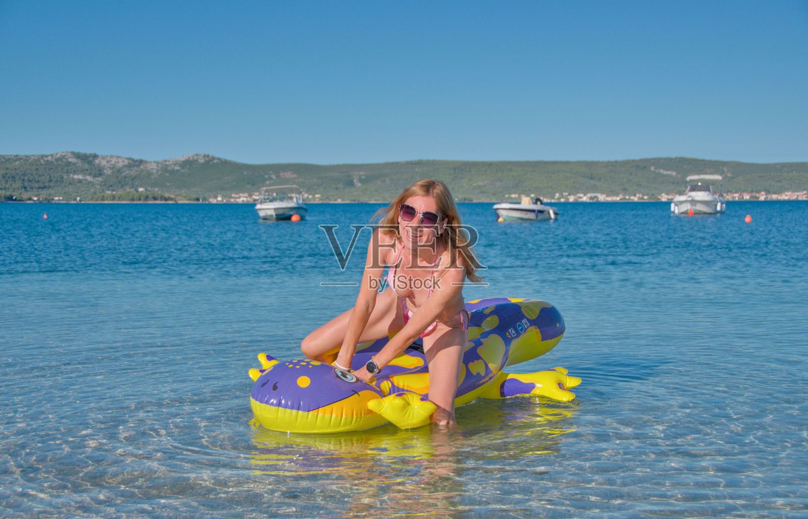 穿着粉红色泳衣的女孩在海上充气玩具上游泳照片摄影图片