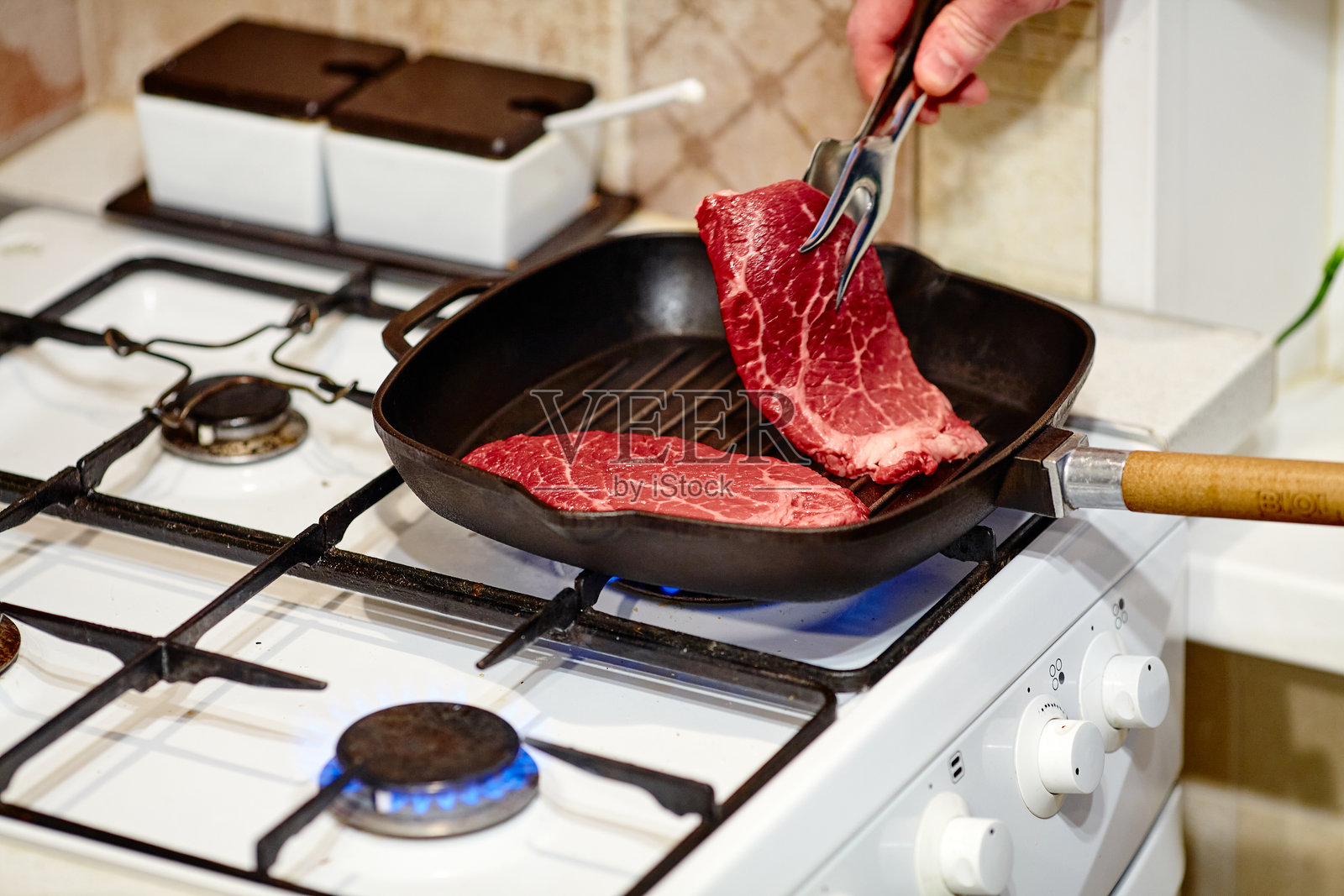 煎锅中烹饪两块牛排的过程，男厨师的手正在给生肉撒盐，特写照片摄影图片