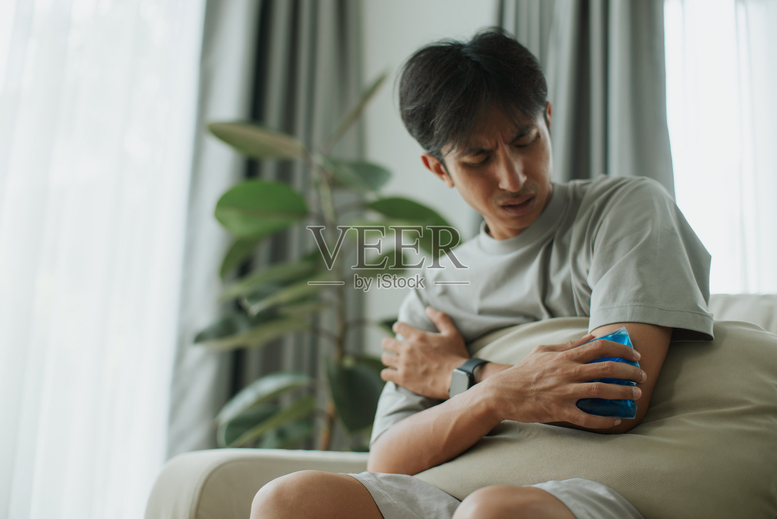 男人将凉爽的凝胶包敷在疼痛的肘部。照片摄影图片