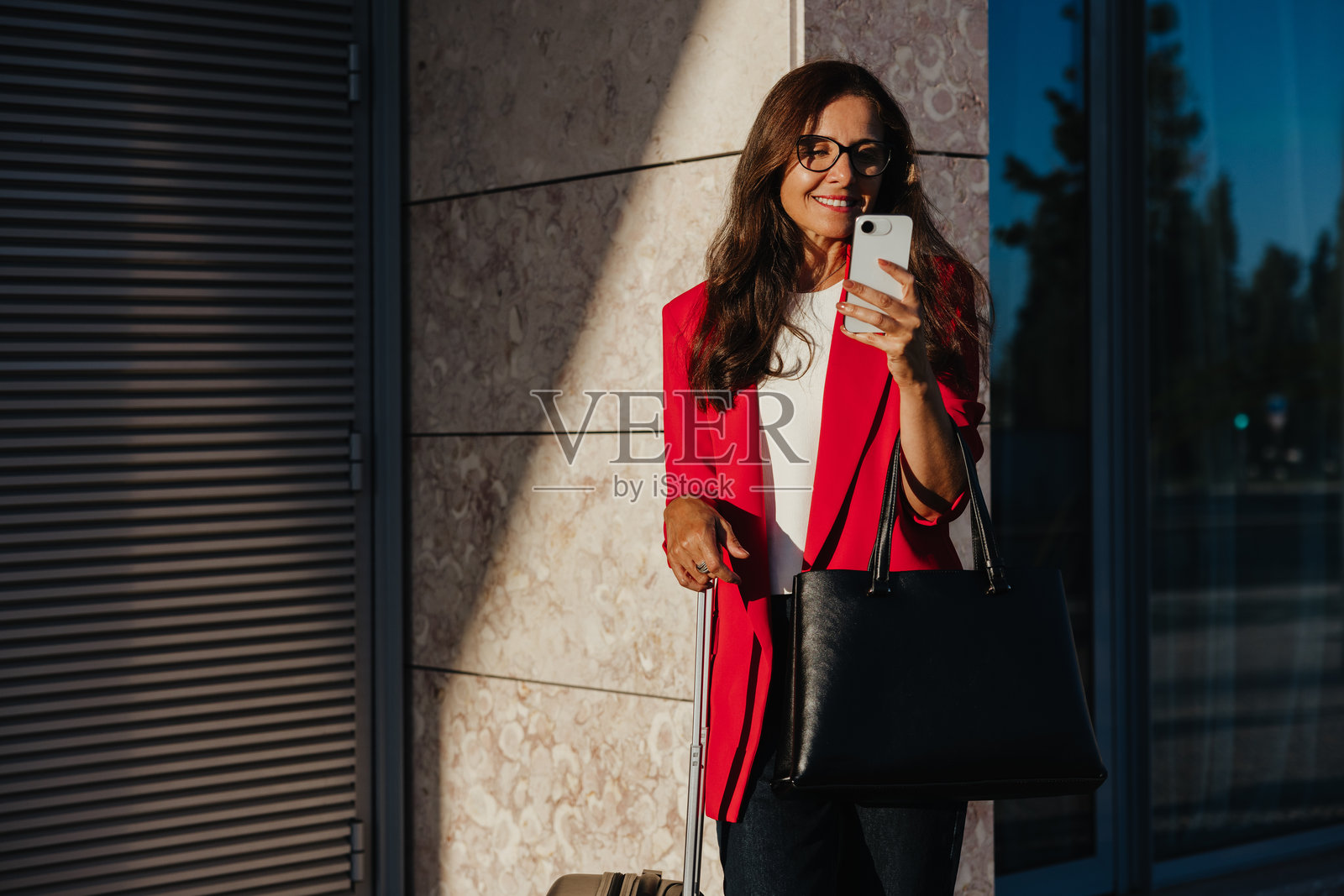 一位女商人在建筑物附近，面带微笑地查看手机照片摄影图片