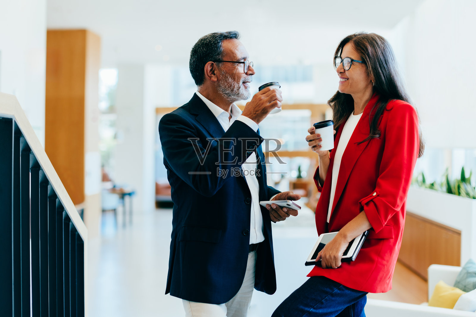 两位资深专业人士在明亮的办公室空间里一边喝咖啡一边交谈照片摄影图片