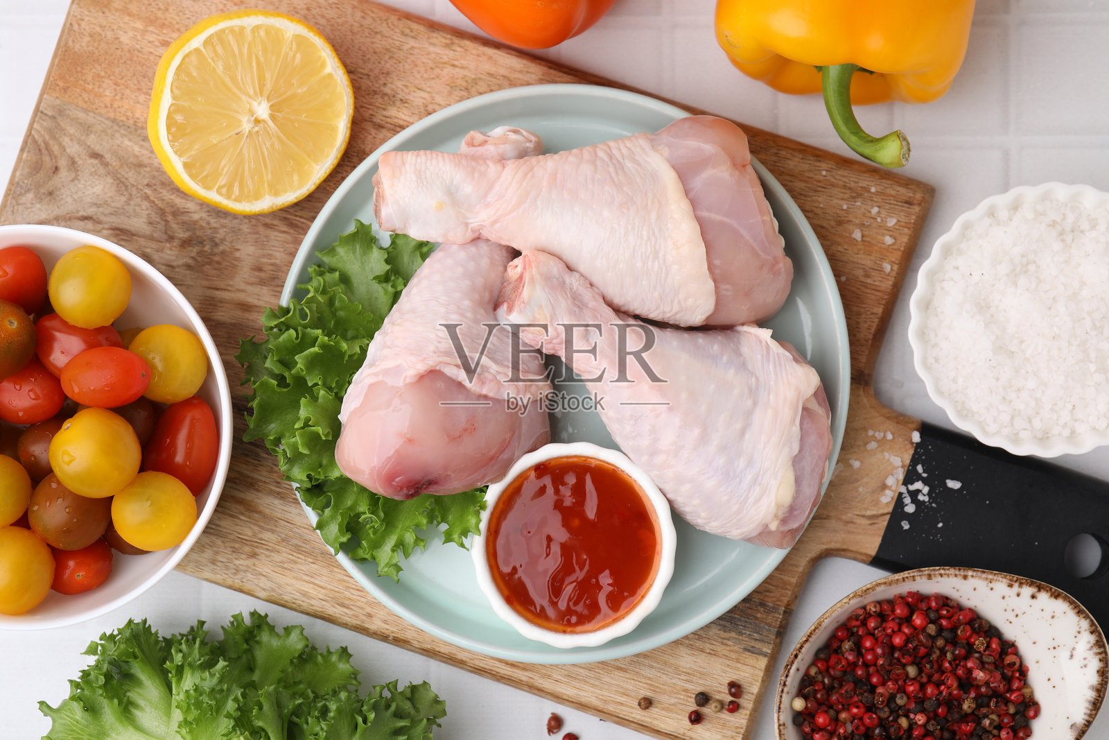 白色瓷砖桌面上，生鸡腿和腌料的俯视构图照片摄影图片