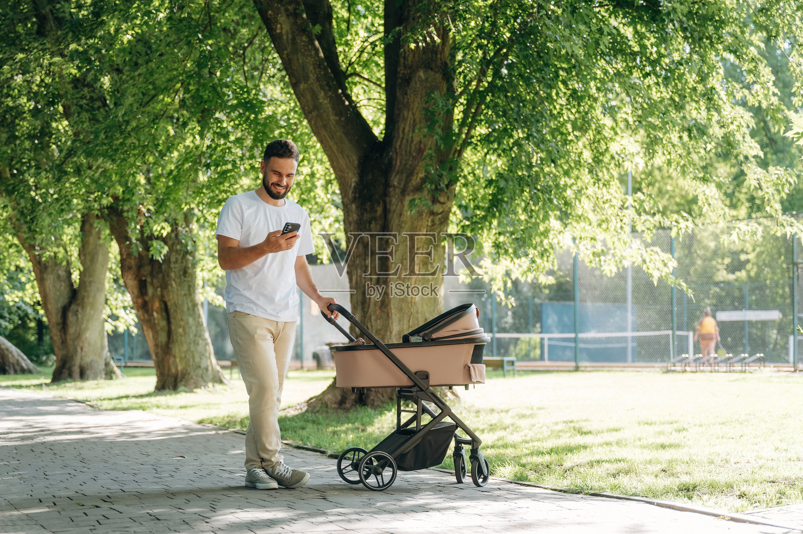 父亲推着婴儿车在公园散步，同时使用智能手机照片摄影图片