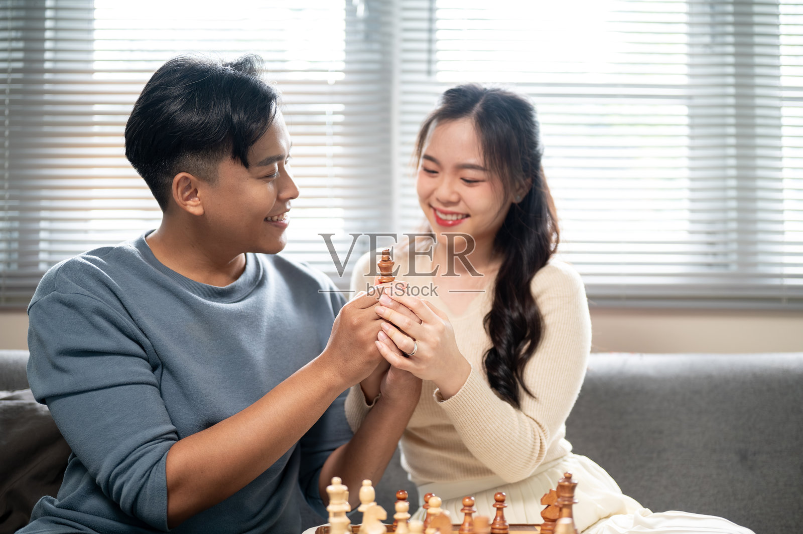 亚洲男女在家里的沙发上，一起拿着棋子放在木制棋盘上照片摄影图片