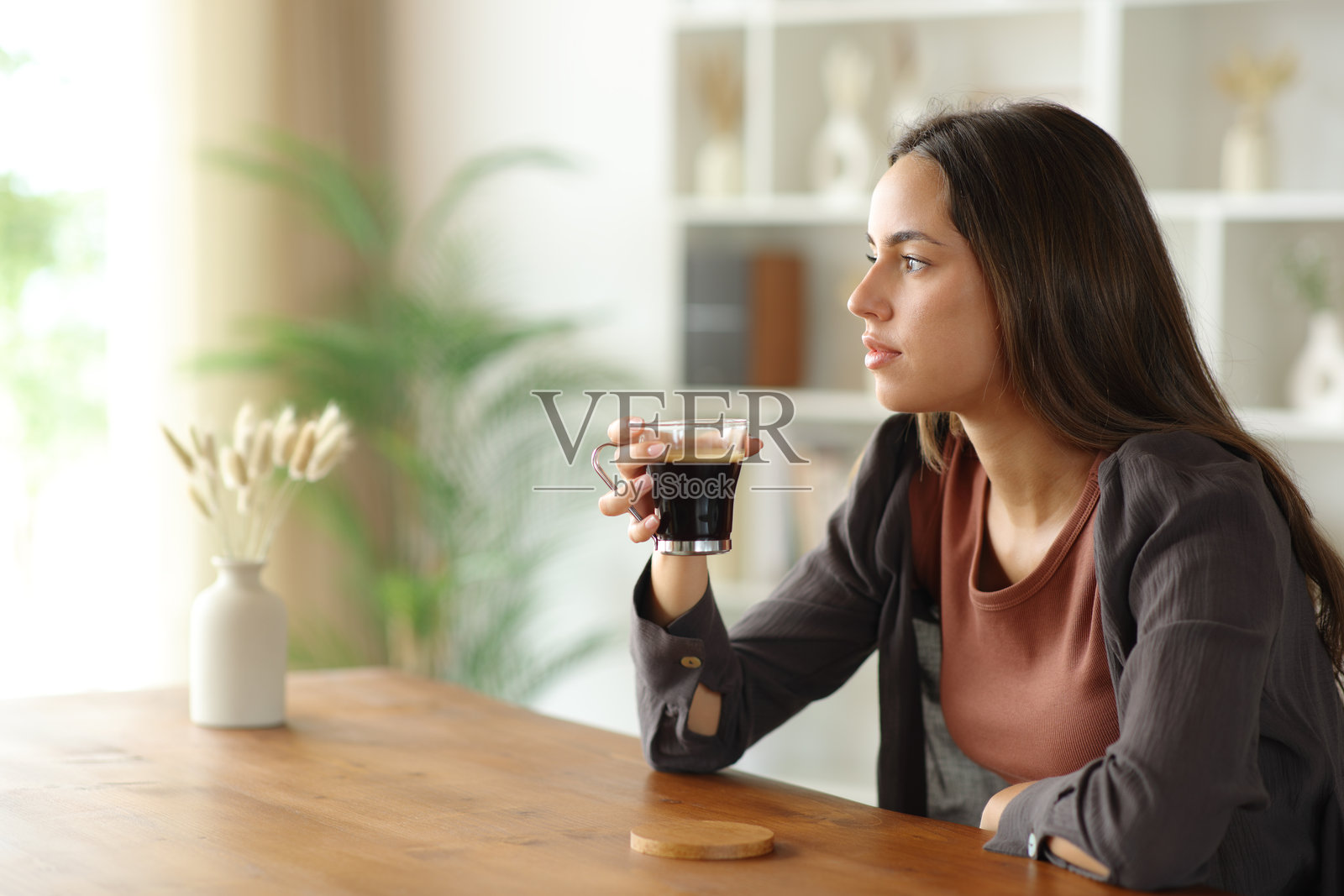 一位心不在焉的女士，手持咖啡杯，望向别处照片摄影图片