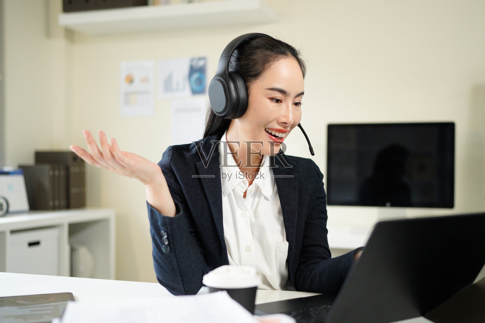 一位职业女性，作为呼叫中心顾问，使用笔记本电脑提供客户服务、支持或咨询。这位专业的亚洲顾问或快乐的客服代表戴着耳机，通过电脑处理联系我们或电子商务事宜。照片摄影图片