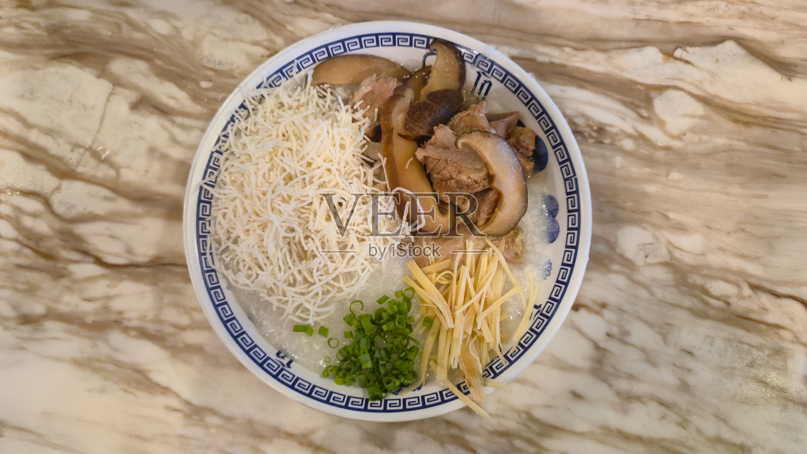 大理石桌上的碗装米粥，配有蘑菇、姜丝和葱花照片摄影图片