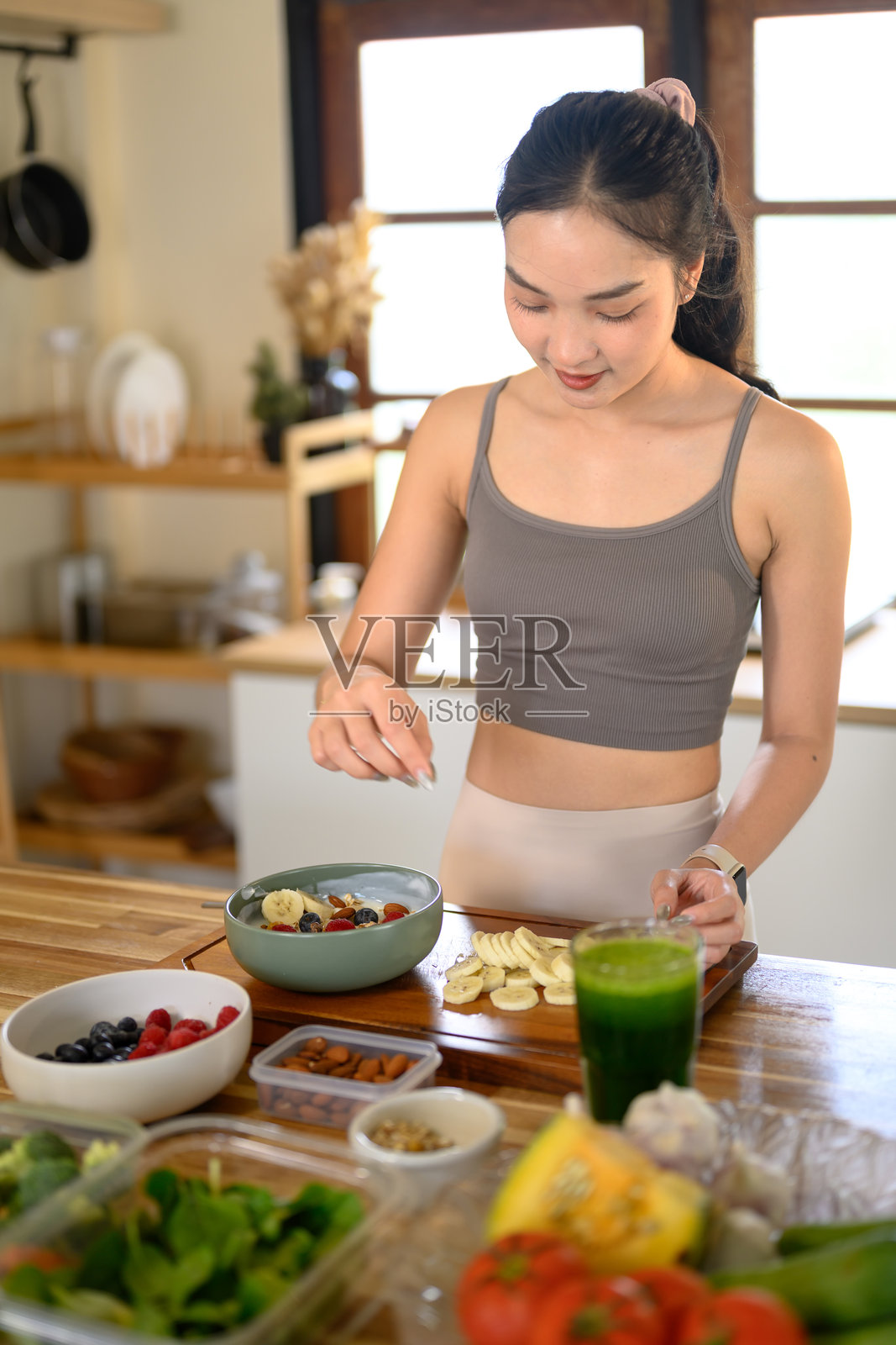 身着运动服的女性正在准备健康的酸奶碗，上面点缀着新鲜水果、坚果和种子，作为营养早餐。照片摄影图片