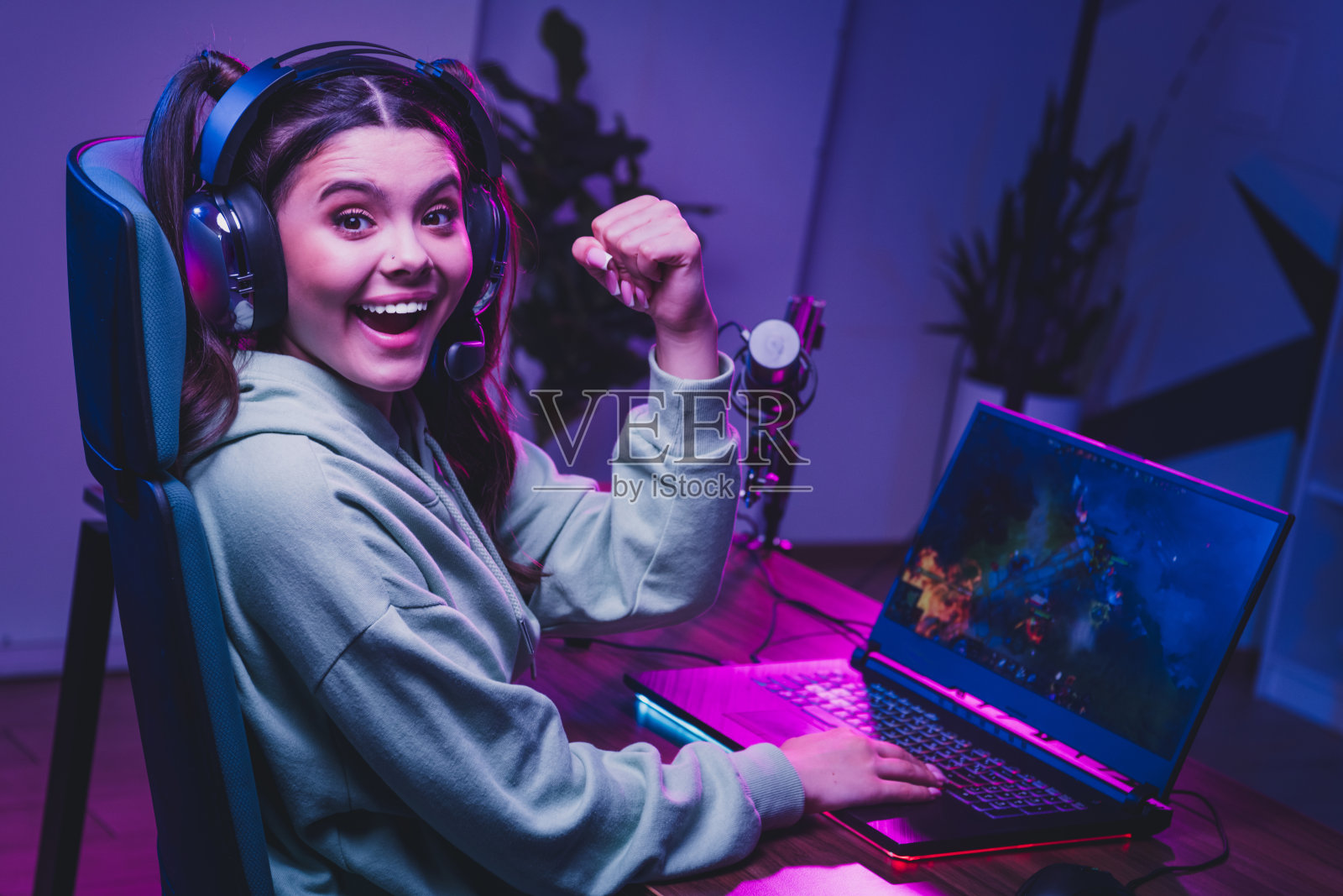 一位快乐的女玩家在霓虹灯装饰的游戏设置中直播视频游戏时庆祝成功照片摄影图片