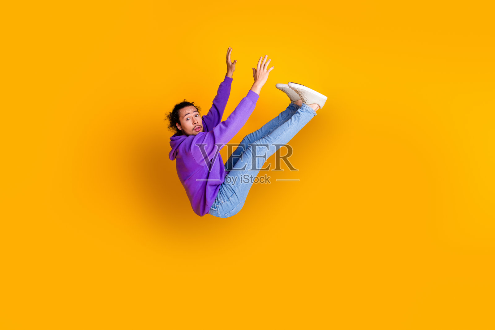 身穿紫色连帽衫的年轻男子在充满活力的黄色背景前腾空而起，展现创意表达和潮流休闲时尚照片摄影图片