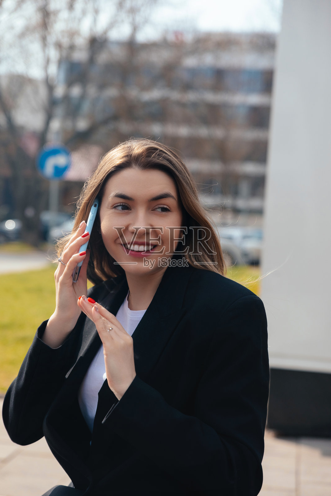 白天晴朗的天空下，一位年轻女子在城市环境中愉快地用手机交谈照片摄影图片