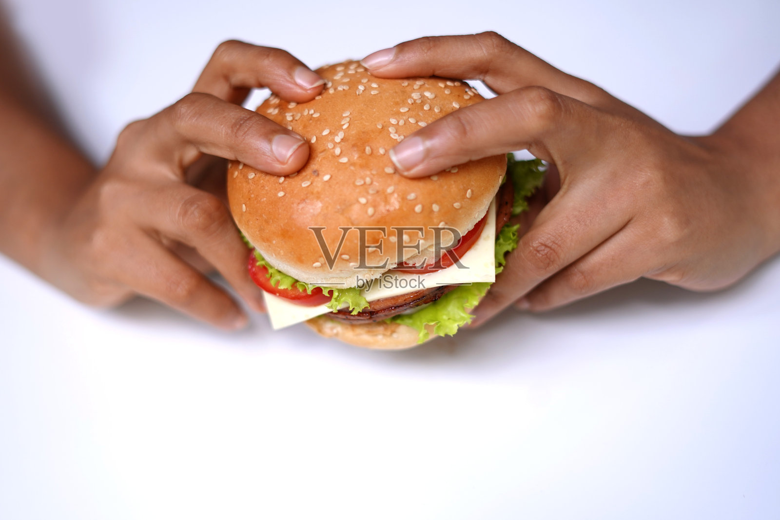 在吃第一口之前，手拿着汉堡包，背景为白色。美食摄影。照片摄影图片