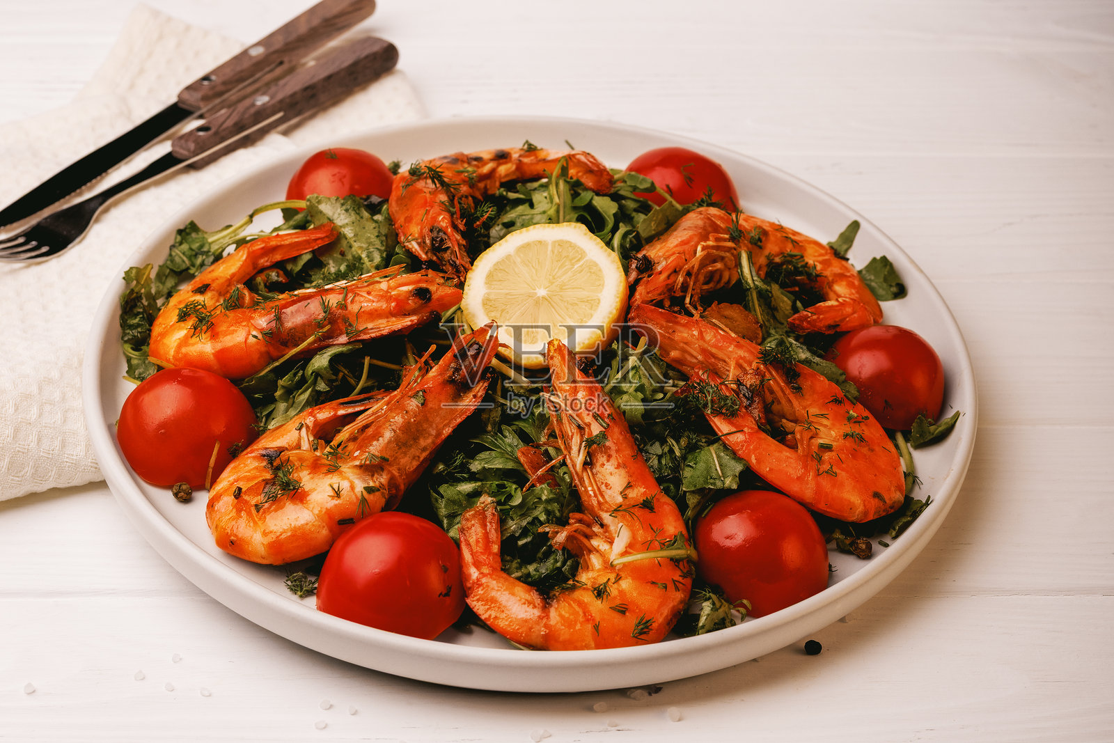 盘子里的沙拉，配有大虾、绿叶蔬菜、番茄和柠檬照片摄影图片