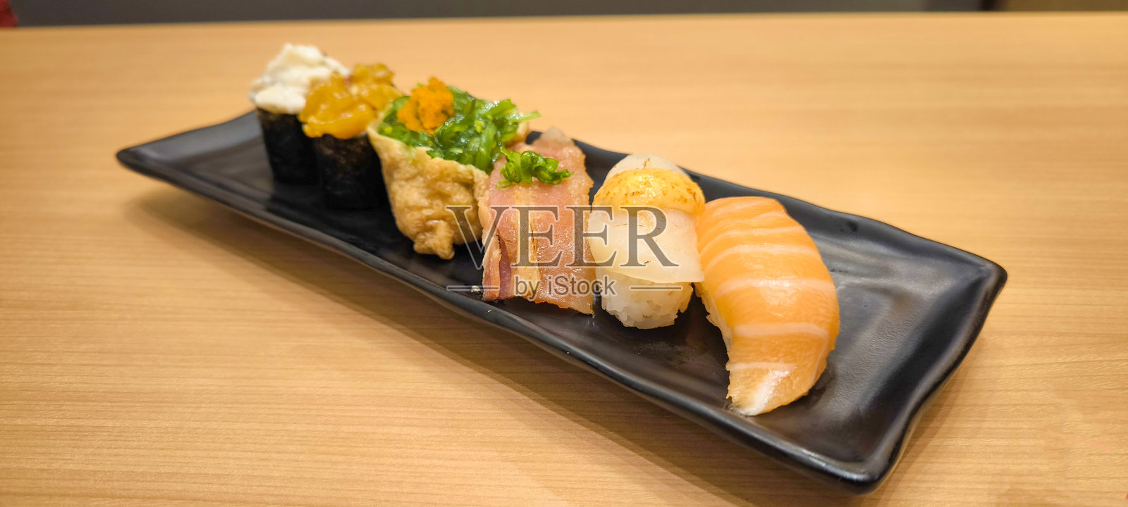 寿司放在黑盘中，置于木桌之上照片摄影图片