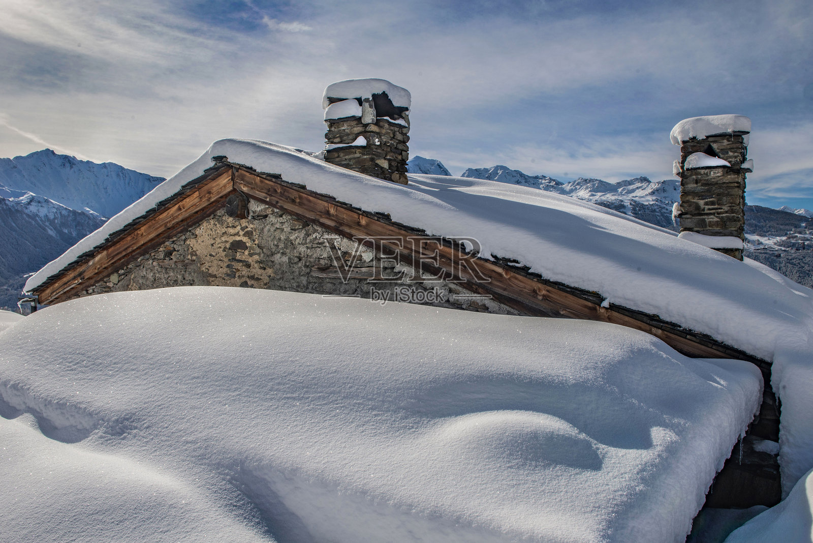 阿尔卑斯小木屋的屋顶和烟囱覆盖着新鲜的雪，坐落在山中。照片摄影图片