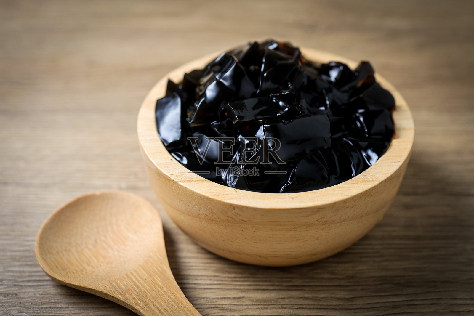 一个装满晶莹剔透黑色仙草冻方块的木碗放在木桌上。照片摄影图片