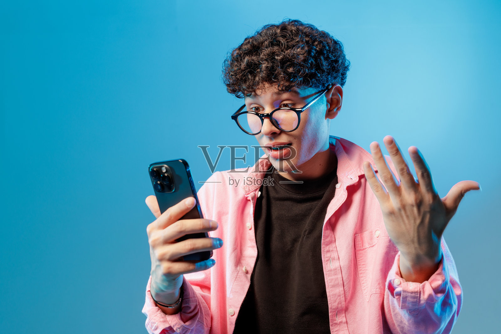 一名青少年在演播室里通过智能手机进行视频聊天，表情惊讶照片摄影图片