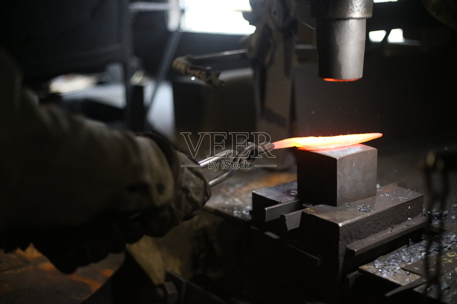 一位工匠正在将加热的材料锻造成形照片摄影图片