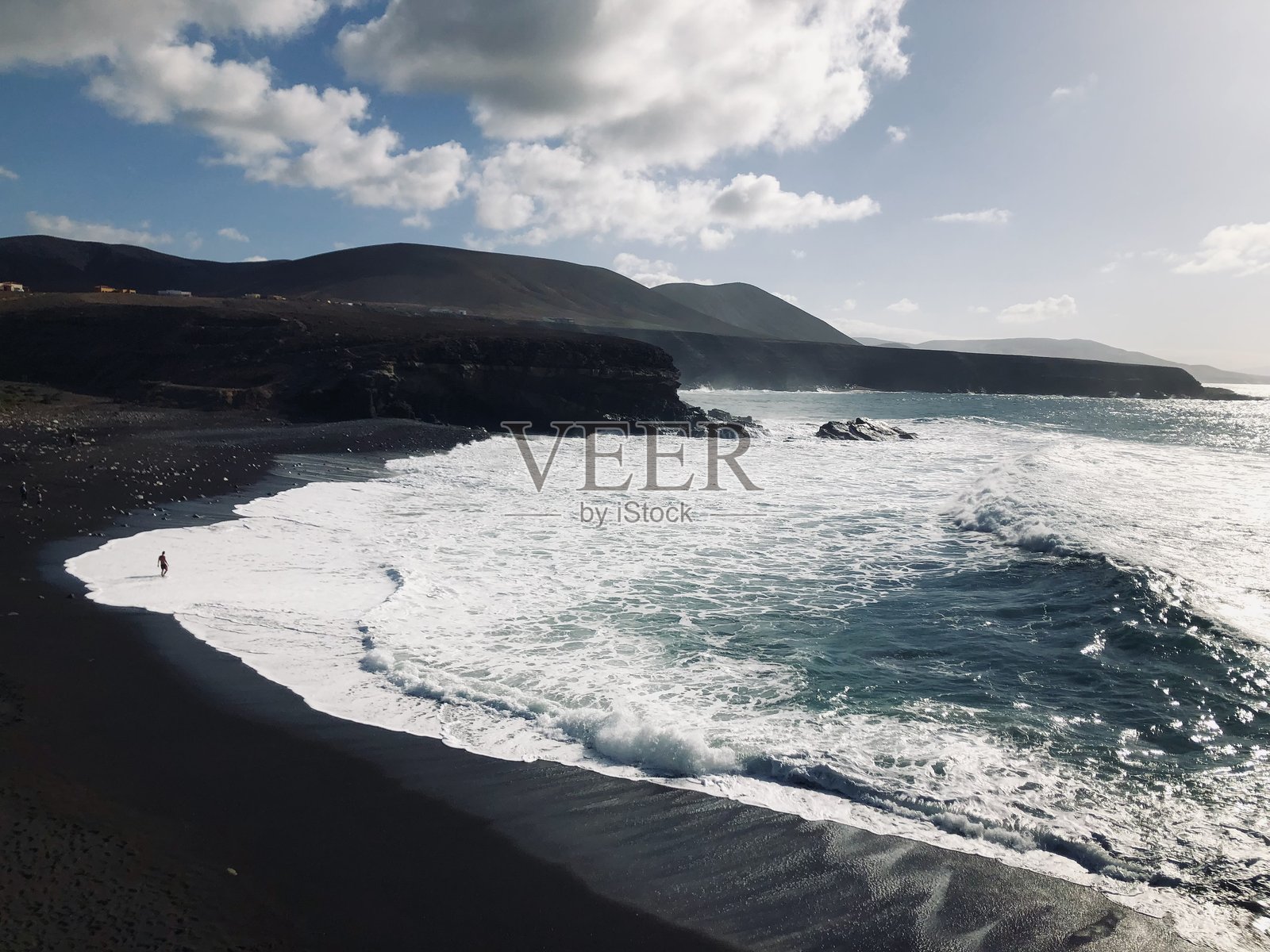 黑色的海滩、白色的海浪和海滩上的人。照片摄影图片