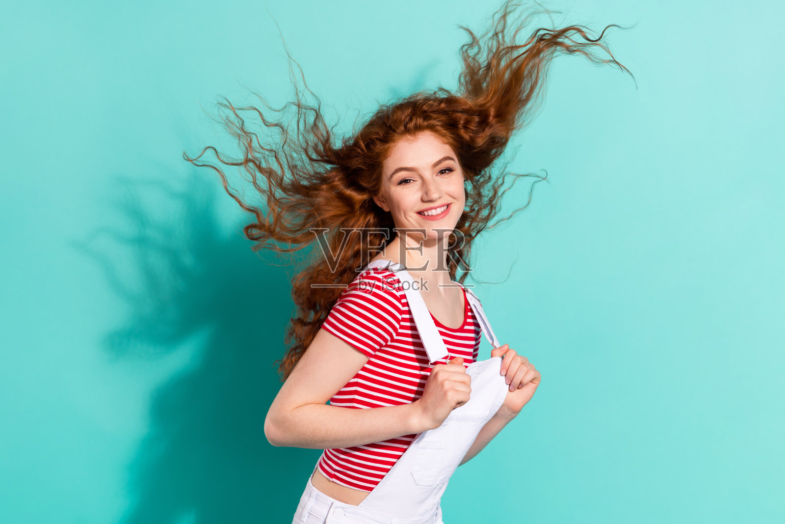 身穿休闲服饰、头发被风吹拂的迷人快乐女孩肖像，背景为鲜艳的蓝色照片摄影图片