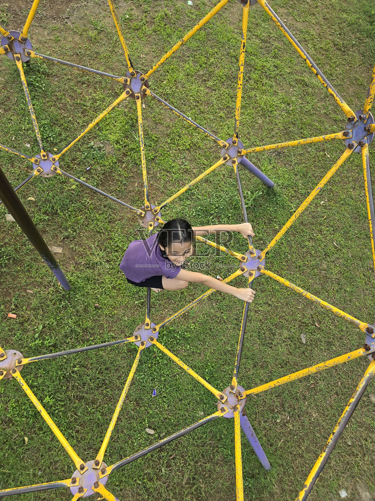 一个小女孩正在攀爬游乐场设施，她专注而用力地抓住金属栏杆，营造出愉快的户外氛围照片摄影图片