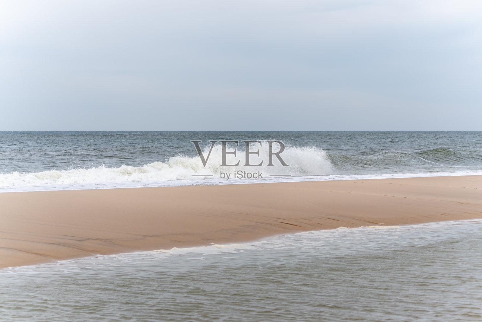 平静的天空下，温柔的海浪轻轻拍打着空旷的沙滩。照片摄影图片