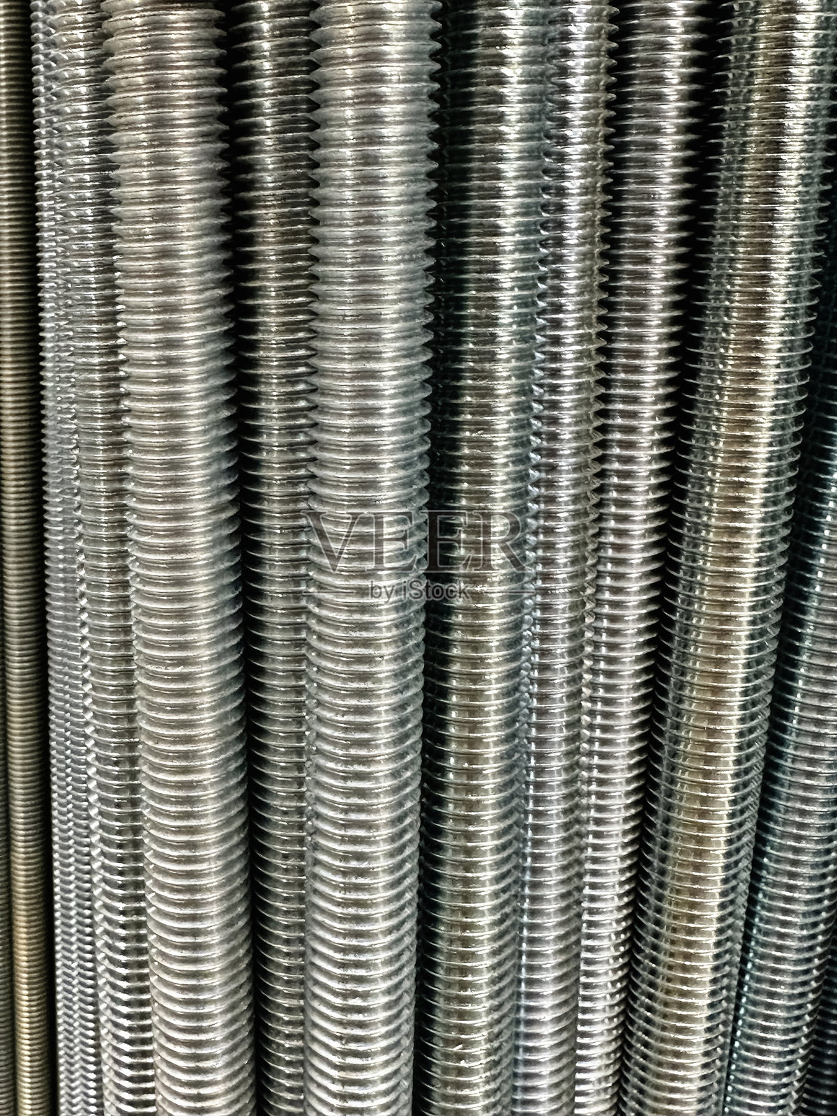 各种长度和直径的螺纹金属杆的垂直排列，用于建筑和组装的光亮钢制紧固件照片摄影图片