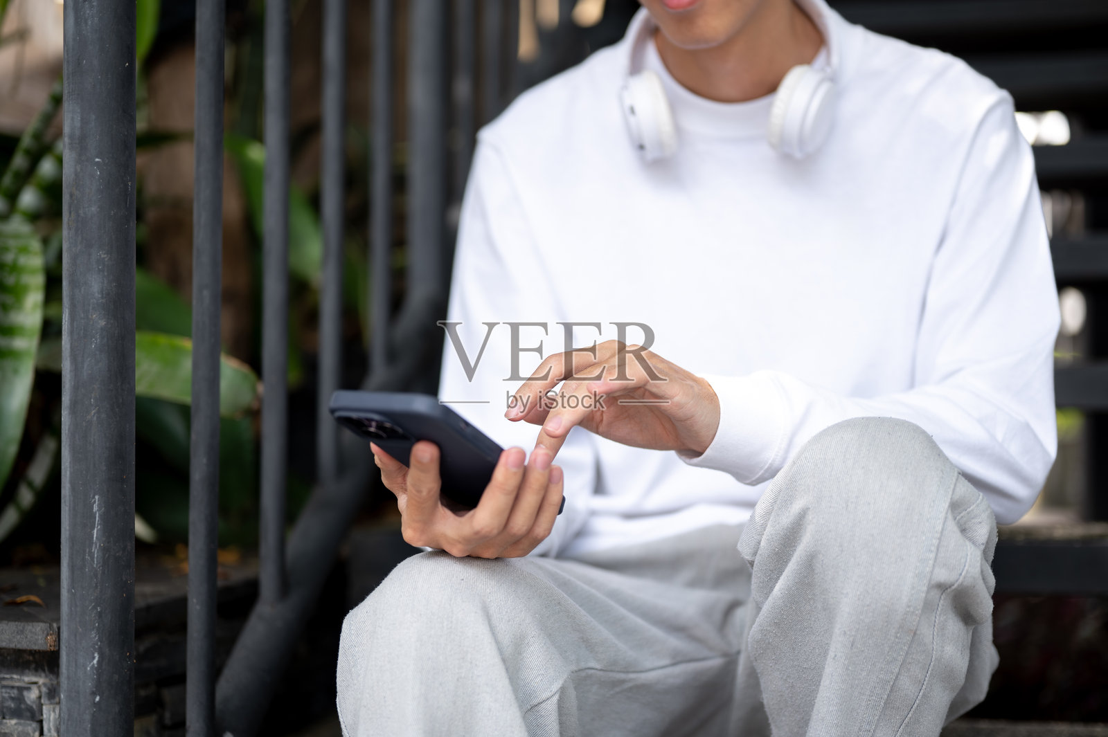 一个男人坐在户外花园咖啡馆的金属楼梯上，一边看手机一边打字。照片摄影图片