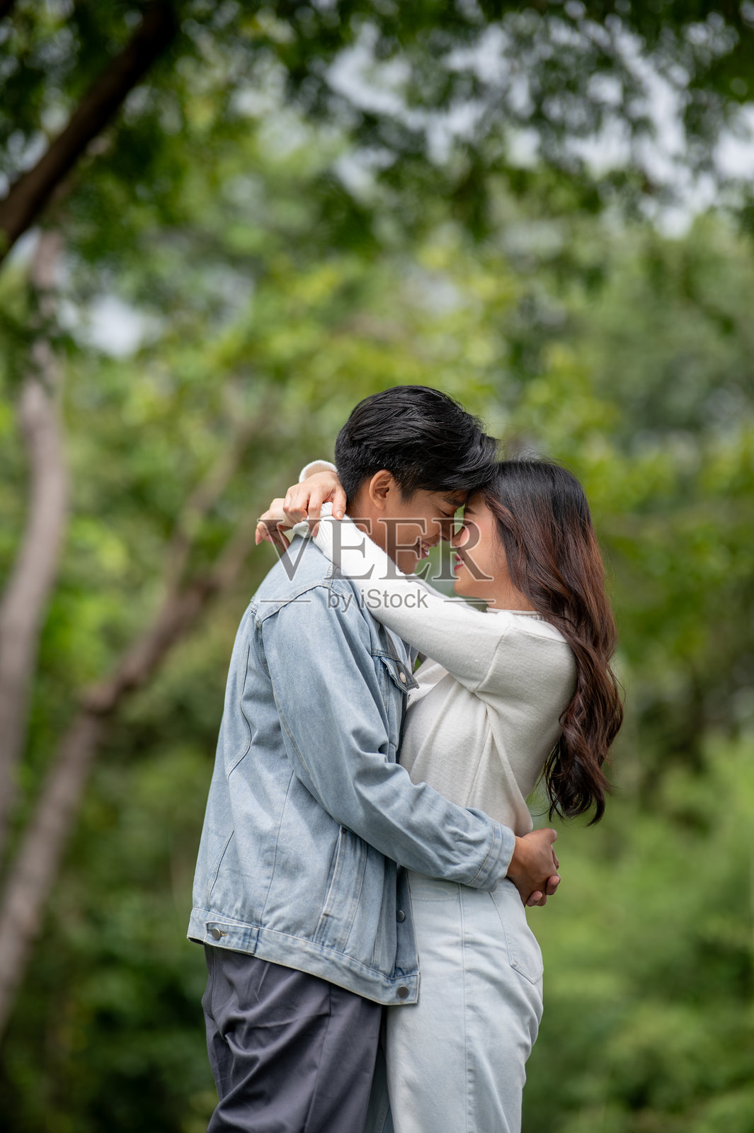 一对年轻的亚裔情侣，一男一女，头碰着头，互相拥抱，站在公园的户外。照片摄影图片