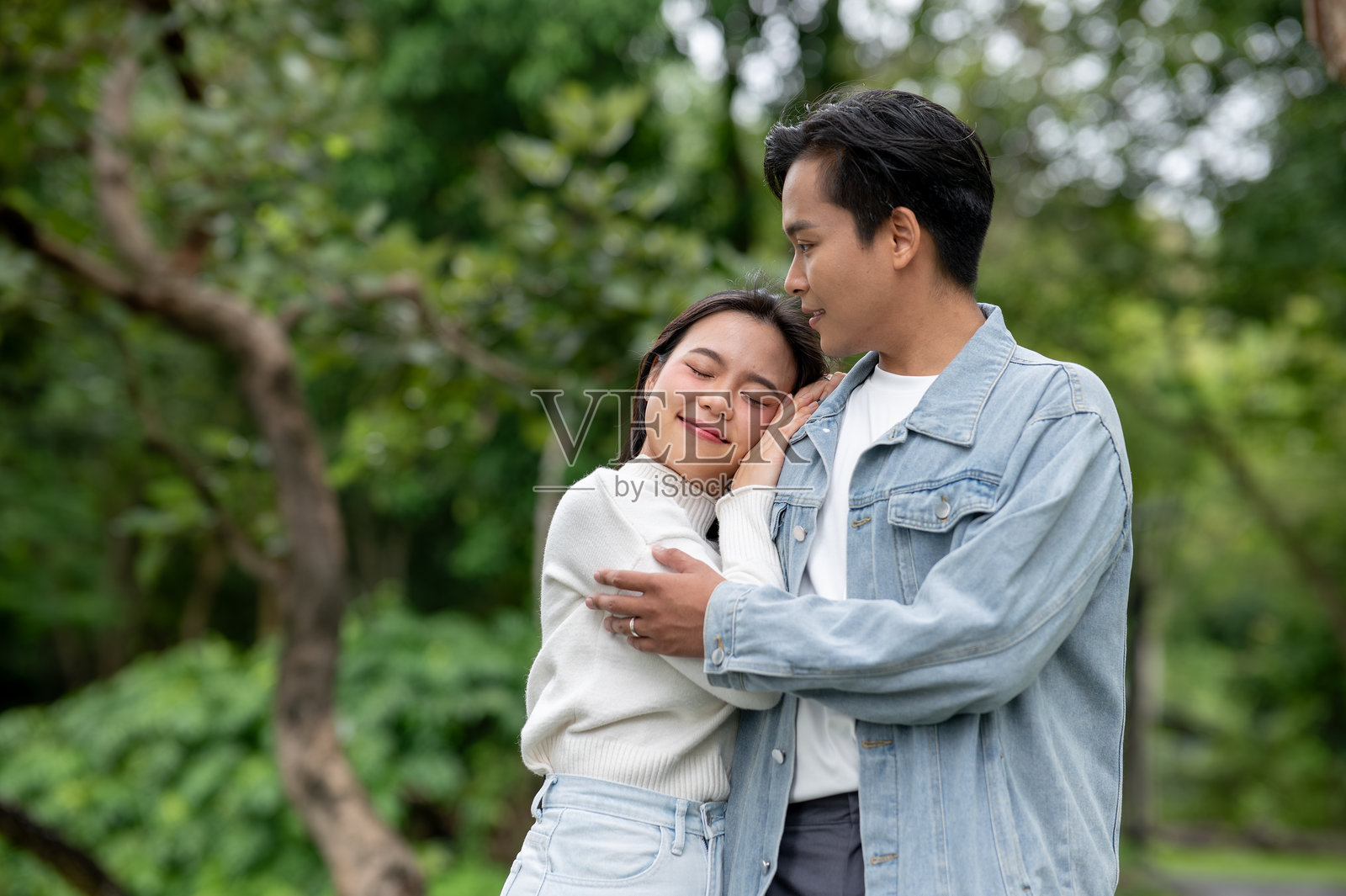 年轻的亚洲情侣，女子靠在男子肩上，两人一同站在公园户外。照片摄影图片