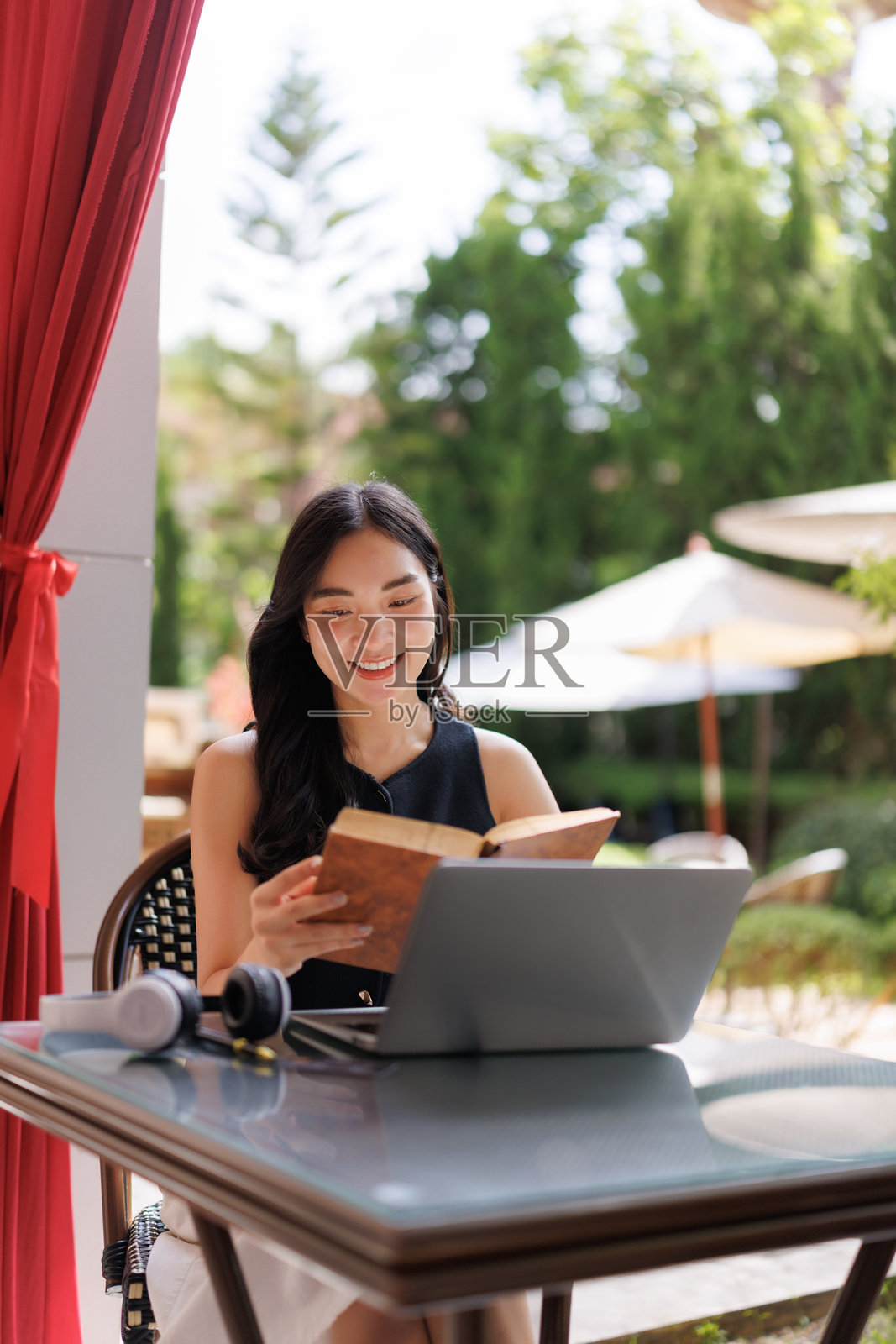 年轻的亚洲女性在户外用笔记本电脑学习，同时阅读一本书照片摄影图片