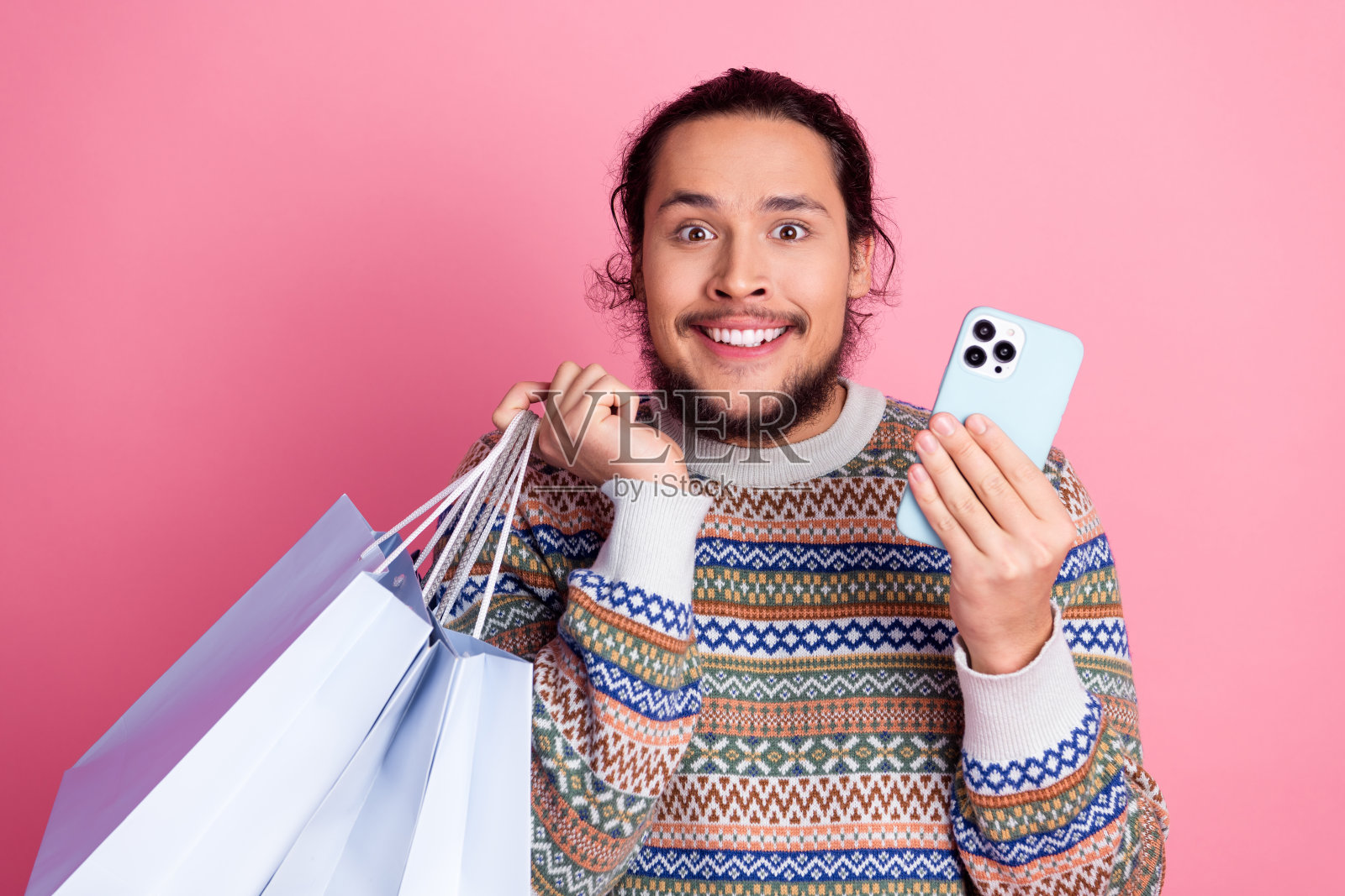 一个兴奋的男人，一手拿着购物袋和智能手机，背景为粉色，他兴高采烈地展示着休闲时光照片摄影图片