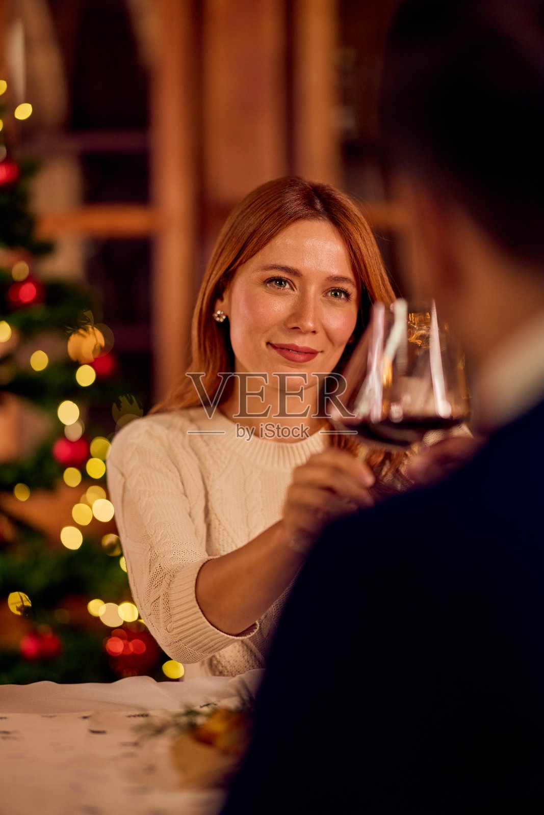 朋友们在节日树旁举杯庆祝温馨的圣诞晚餐，伴有美酒照片摄影图片