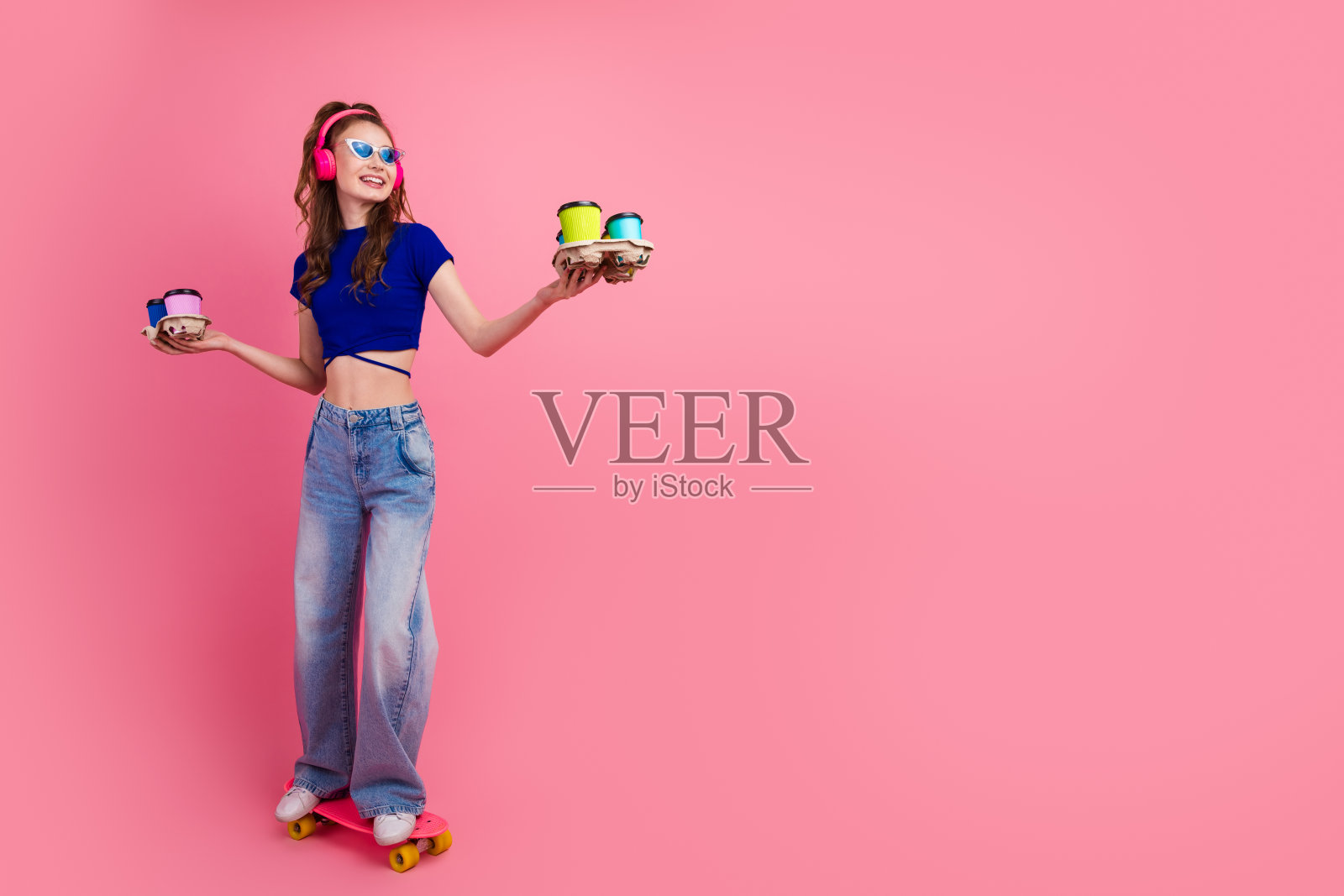 身穿旱冰鞋的活力四射的年轻女子，手持色彩缤纷的饮品，背景是鲜艳的粉色。照片摄影图片