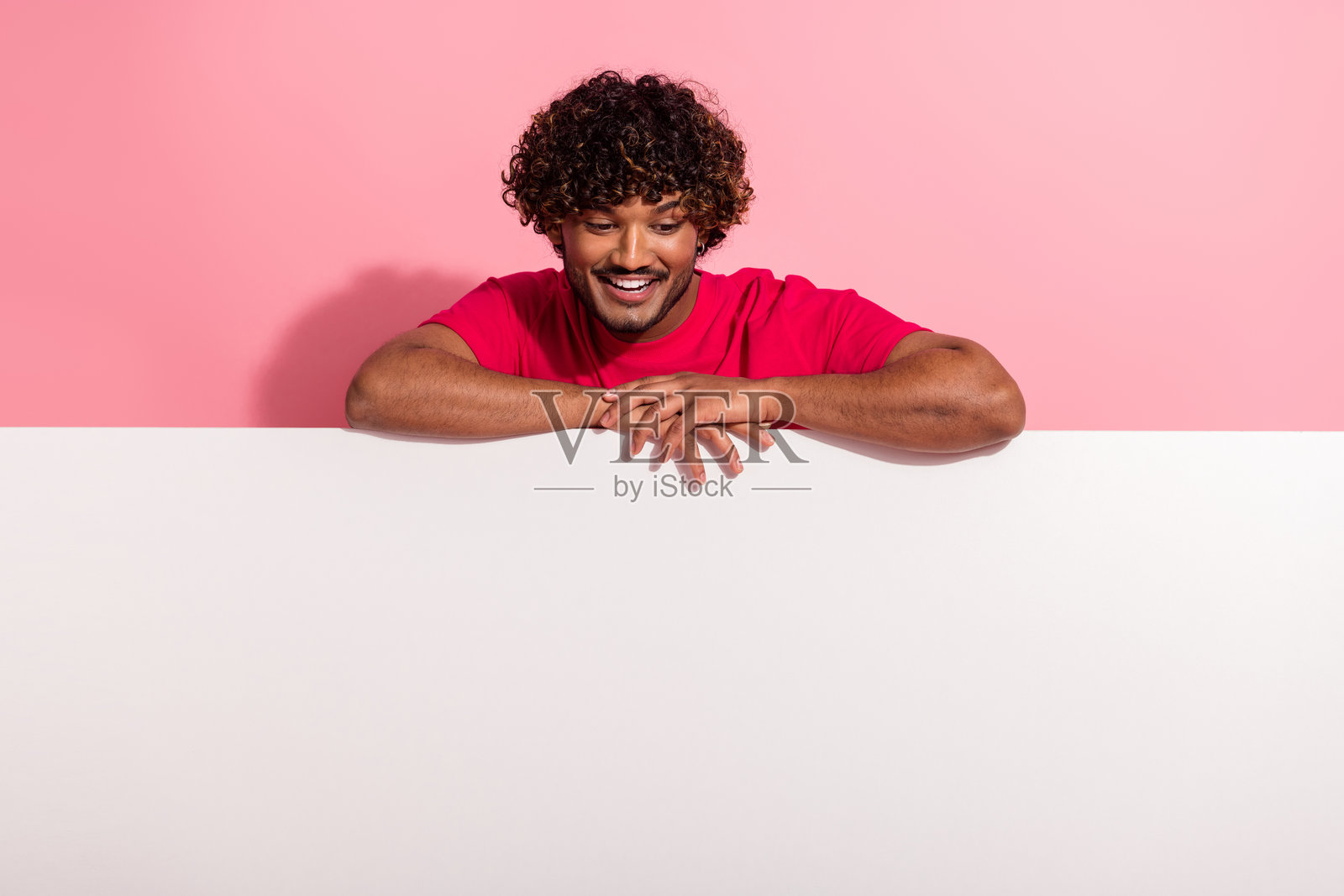 身穿红衣的年轻男子，脸上带着快乐的表情，发型时尚，在色彩鲜艳的背景前摆姿势。照片摄影图片