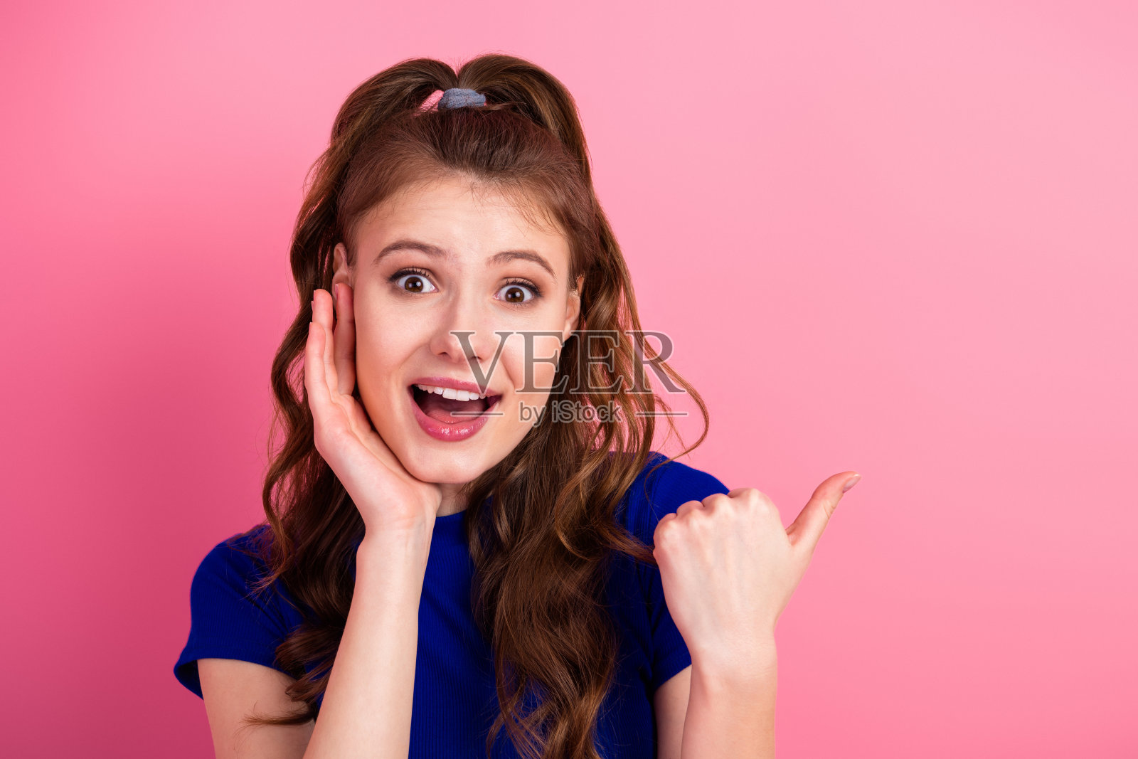 一位年轻时尚的女子身穿蓝色上衣，充满活力的自信表情，在粉色背景前摆姿势。照片摄影图片