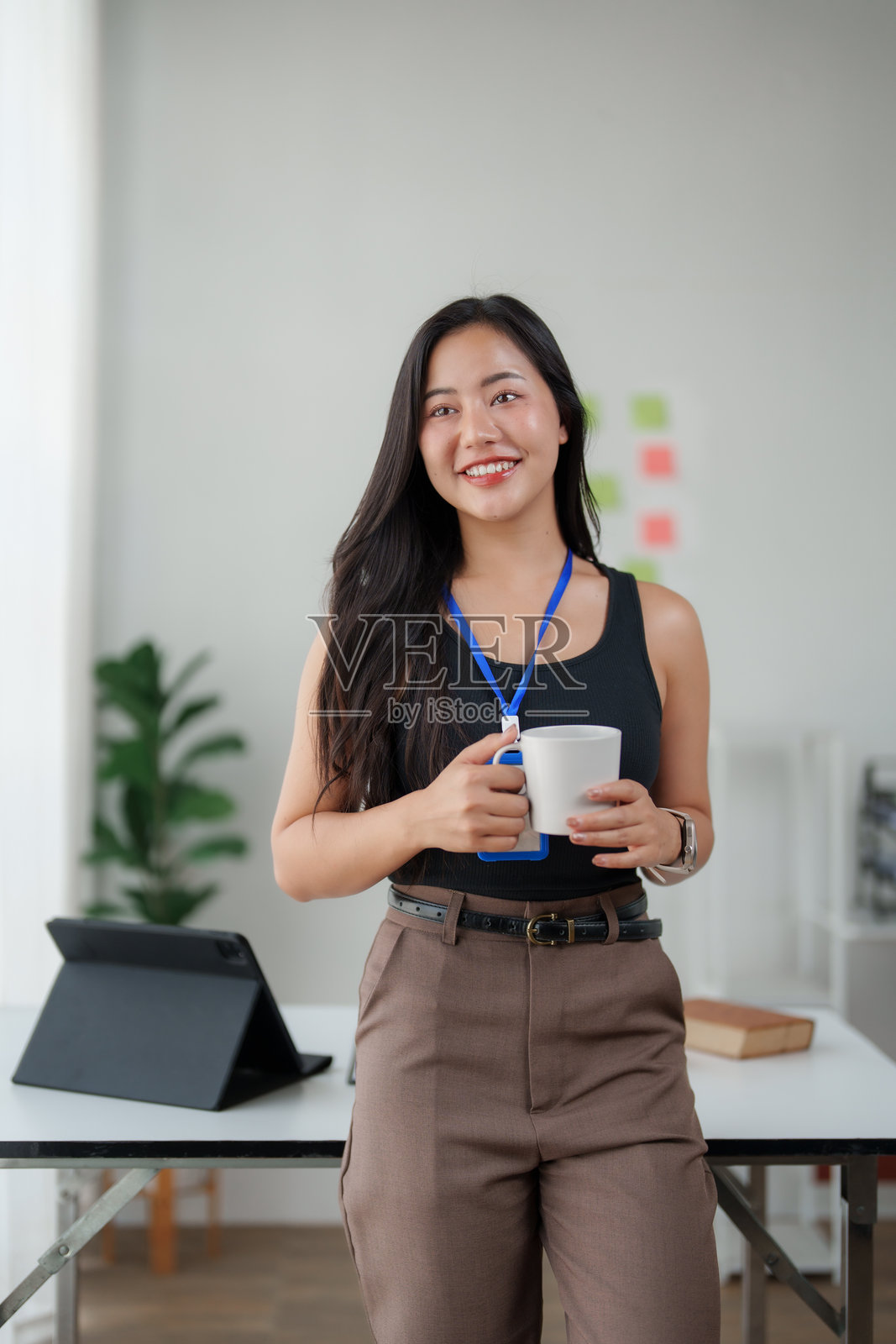 一位年轻的亚洲女商人面带微笑，在办公室里拿着咖啡杯照片摄影图片