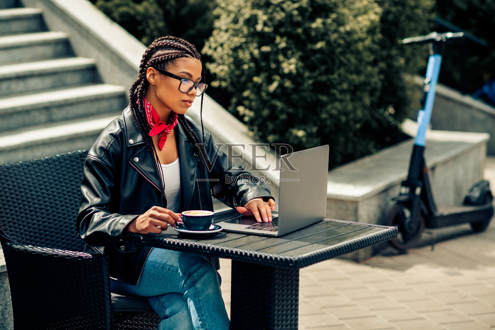 一位年轻女子留着编发，在户外的咖啡馆用笔记本电脑工作，享受休闲时光和都市生活方式照片摄影图片