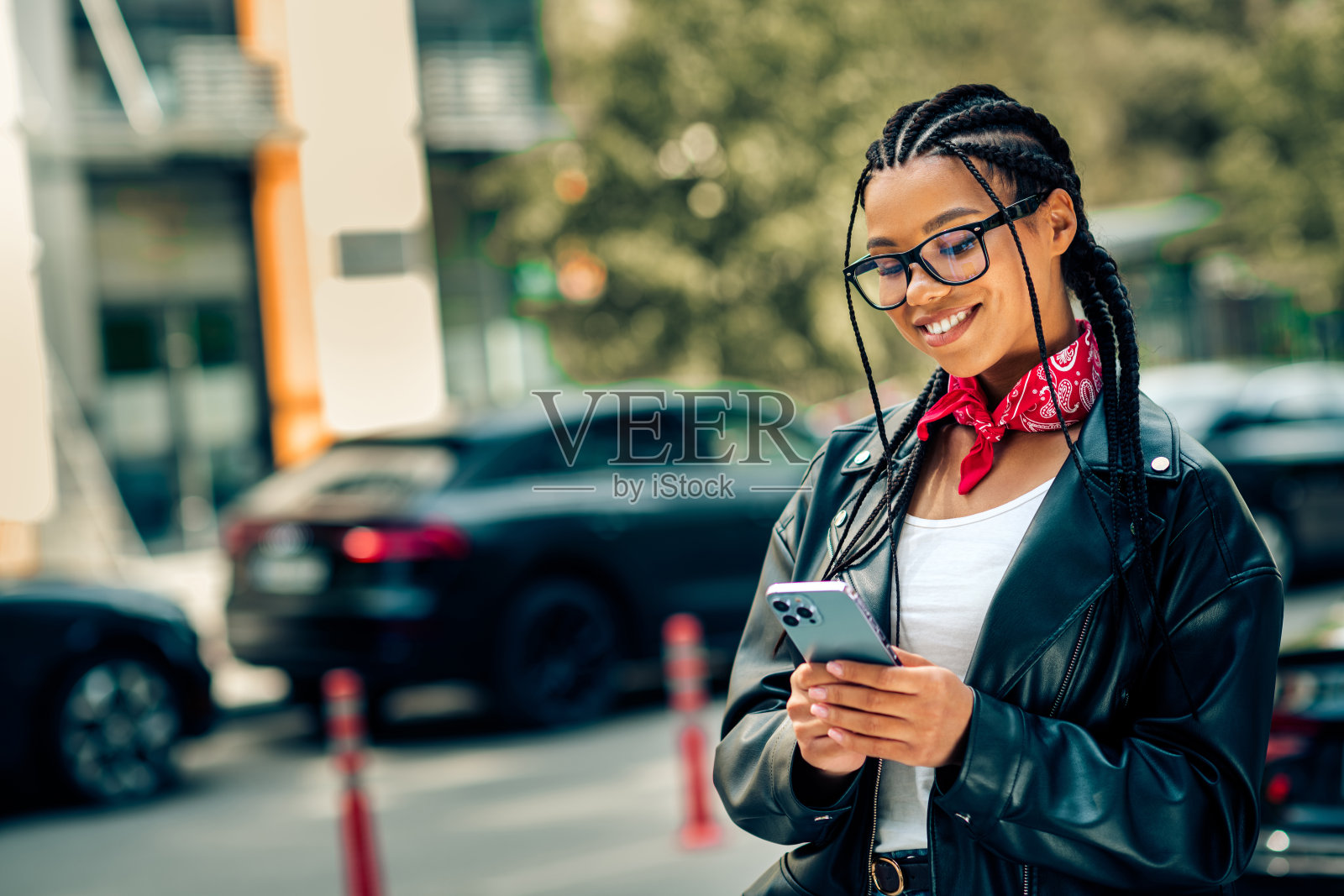 阳光明媚的白天，一位时尚年轻女子在城市街道上边走边笑着使用智能手机照片摄影图片