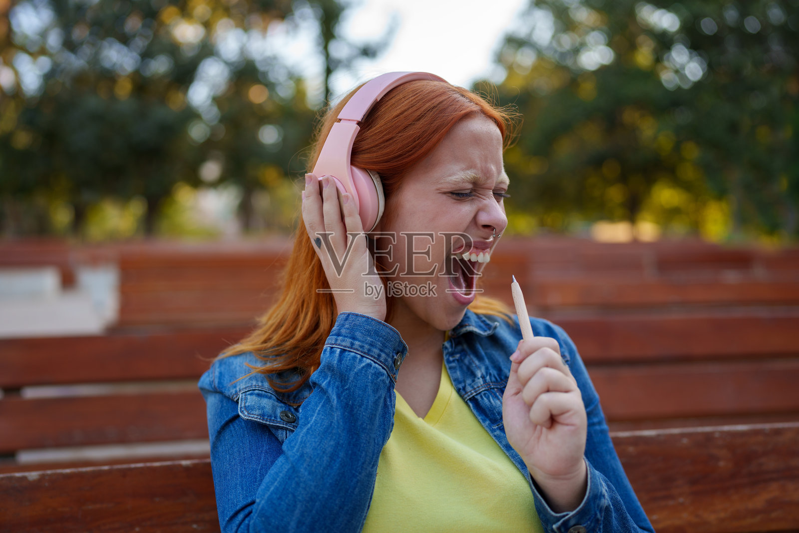 年轻女子在公园里戴着粉色耳机，充满激情地放声歌唱，享受音乐照片摄影图片