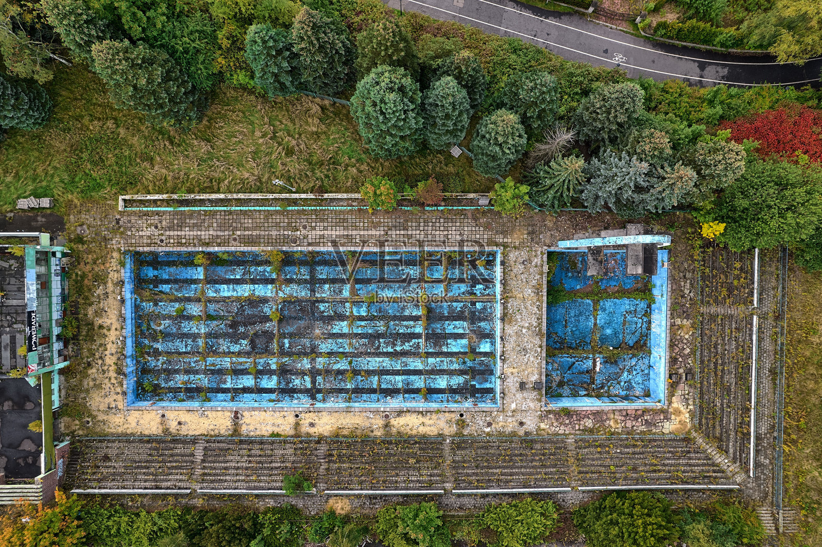 从空中俯瞰废弃的游泳池，蓝色的油漆已经斑驳，周围环绕着色彩斑斓的秋叶，位于波兰卡托维兹-霍茹夫的西里西亚公园，展现了城市衰败和废弃建筑的景象。照片摄影图片