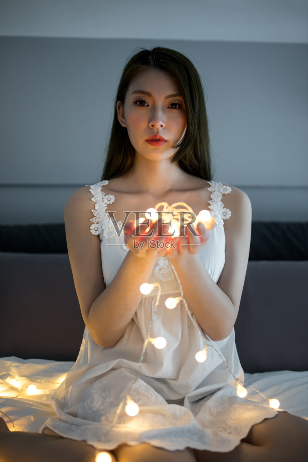 身穿白色蕾丝连衣裙的年轻女子在舒适的环境中手持串灯照片摄影图片