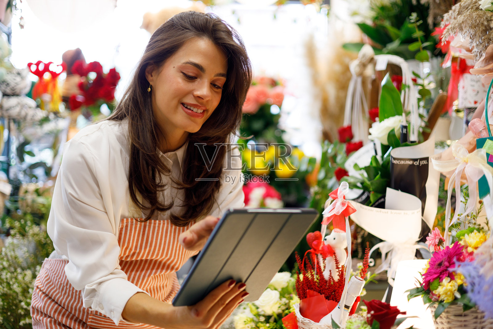 一位女士在花店工作，使用数码平板电脑输入信息，管理小型企业的在线订单和库存照片摄影图片
