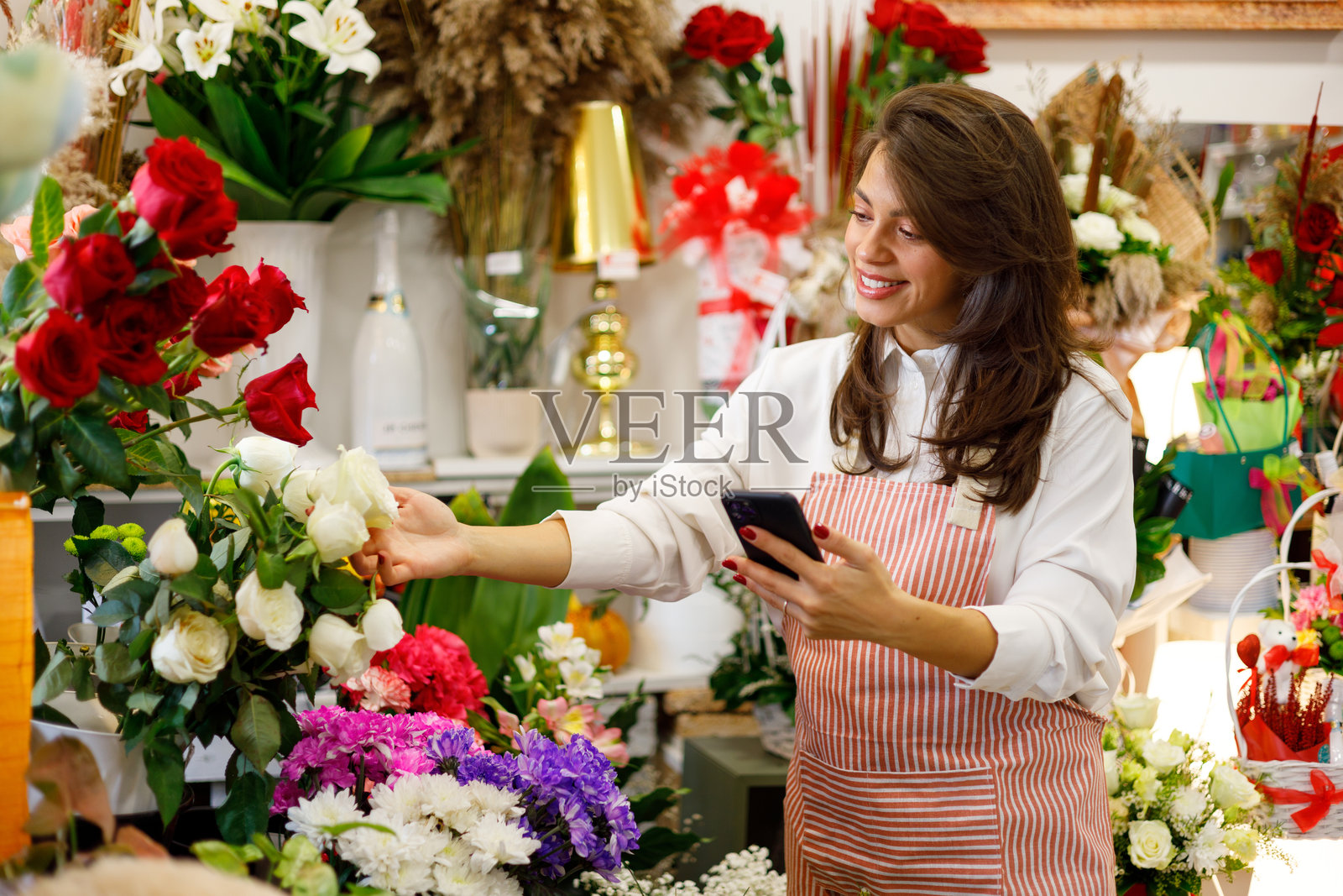快乐的花店女店主正在使用手机，在小型花店里精心布置美丽的鲜花照片摄影图片