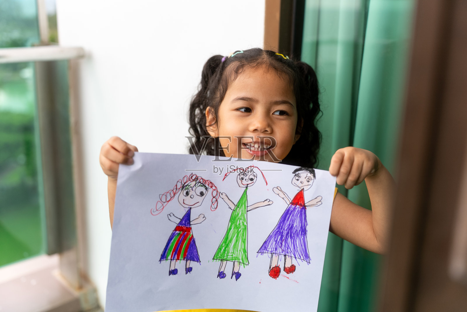 快乐的小女孩在家展示她的绘画作品，用彩色蜡笔在白纸上画画，展现她的想象力，适合学校家庭作业、童年绘画、艺术创作、灵感迸发和儿童艺术学习。照片摄影图片