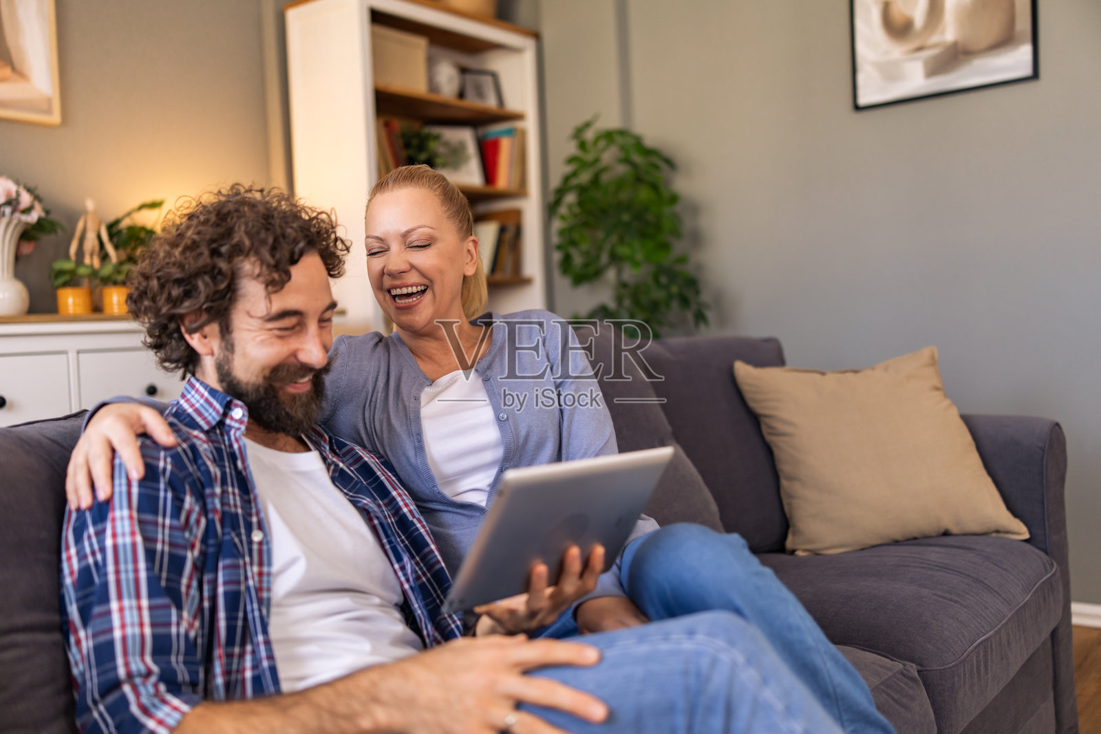 一对情侣坐在客厅的沙发上，看着平板电脑上的搞笑视频，开怀大笑。照片摄影图片